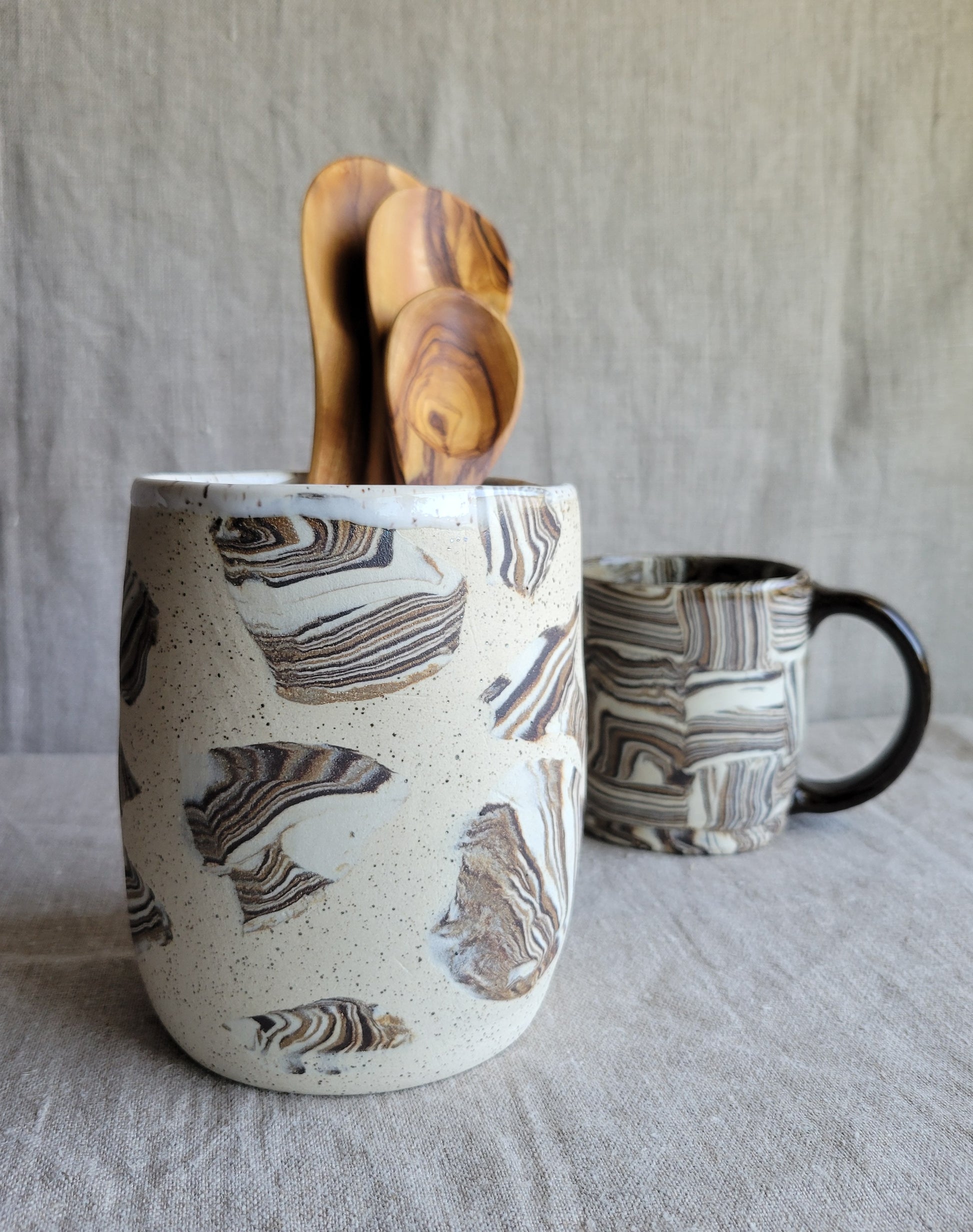 Marble-patterned ceramic mug with wooden utensils on a textured surface