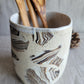 Ceramic utensil holder with abstract pattern containing wooden spoons on a neutral background