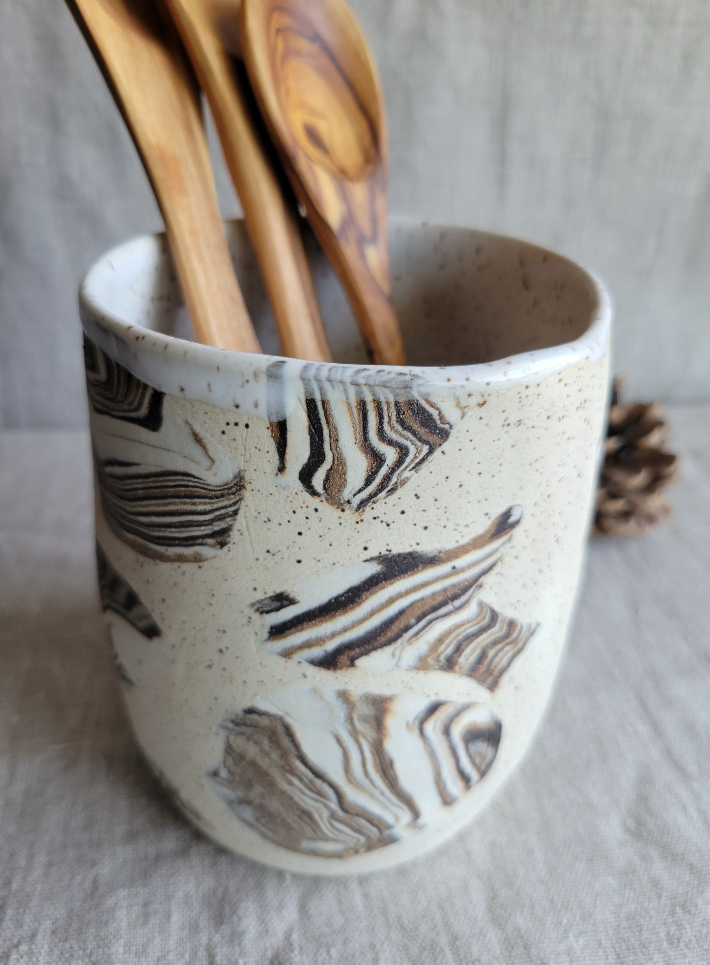 Ceramic utensil holder with abstract pattern containing wooden spoons on a neutral background